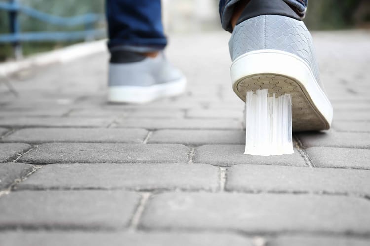 A closeup of a pair of gray shoes on the brick one has gum stuck on it. 
