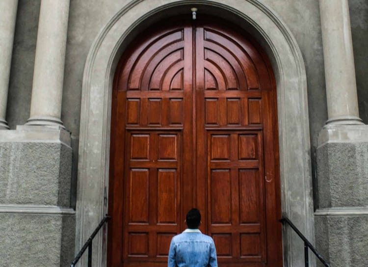 A man looking a big brown wooden door.