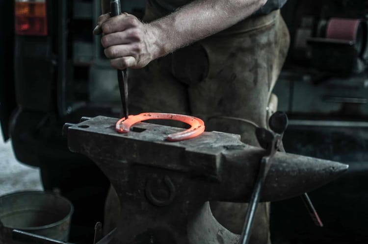 A blacksmith is hammering a horseshoe with a punch.