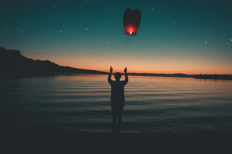A person releases a lantern over a lake at dusk. 