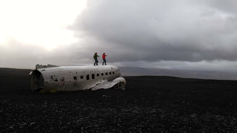 Two men standing on top of an old plane in Iceland with a surfing stance.
