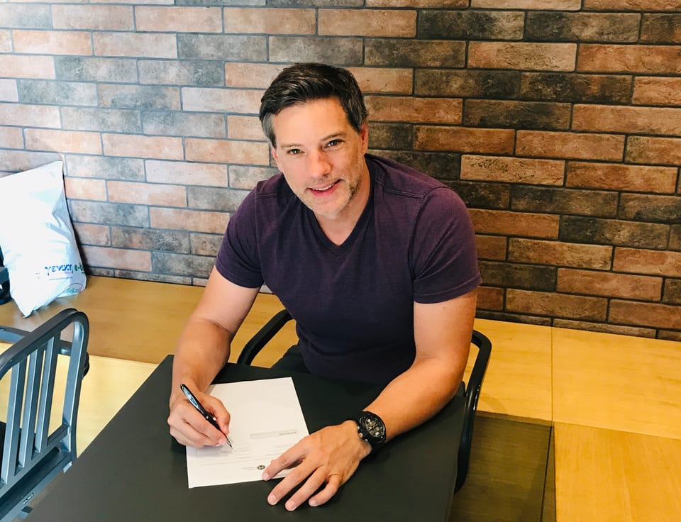 Eric Demeter sitting at a table and signing my book publishing deal at a coffee shop. 