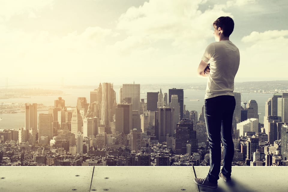 A man is standing on a rooftop and overlooking a city.
