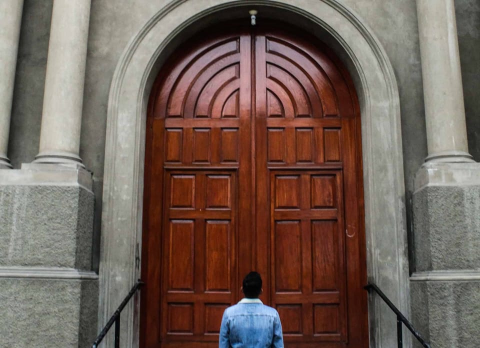 A man looking a big brown wooden door.