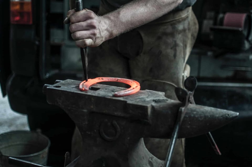 A blacksmith is hammering a horseshoe with a punch.