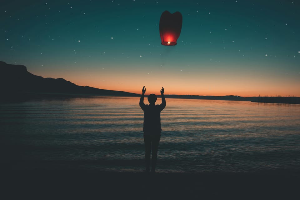 A person releases a lantern over a lake at dusk. 